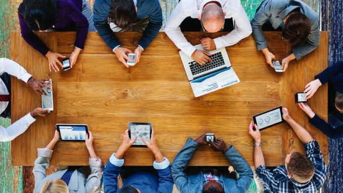 A group of people at a conference table using various mobile devices